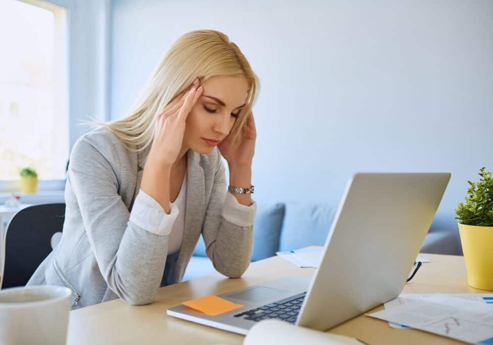 a woman massaging her temples and needs an H pylori treatment while working on her desk